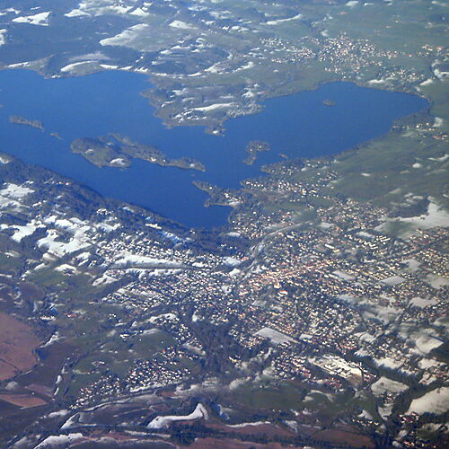 Die Landschaft rund um Murnau Weiter Blick über den Staffelsee bei Murnau mit bewaldeten Ufern, kleinen Inseln und einer hügeligen Landschaft unter bewölktem Himmel.