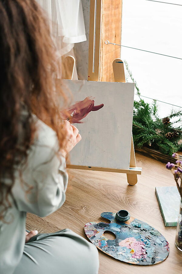 Person arbeitet mit Acrylfarben an einem unvollendeten Bild in ruhiger Atelieratmosphäre.