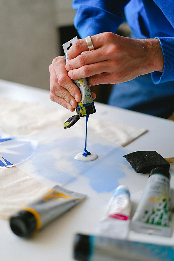 Hand arbeitet mit Pinsel und Acrylfarbe an einer Farbfläche und zeigt den praktischen Umgang mit Material und Farbauftrag.