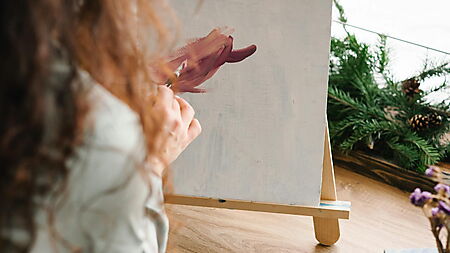 Person arbeitet mit Acrylfarben an einem unvollendeten Bild in ruhiger Atelieratmosphäre.