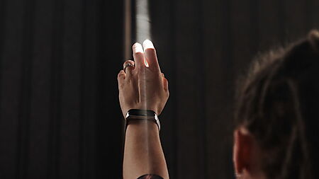 Ausgestreckte Hand, die in einem dunklen Raum nach einem hellen Lichtstrahl greift