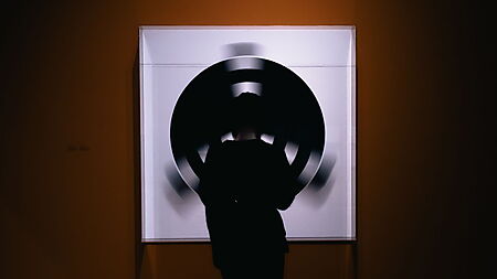 Besucherin steht vor einer großen abstrakten Kreisform in einer Galerie und betrachtet Linien, Formen und Flächen als zentrale Bildelemente.